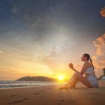 Woman sitting on Mirissa Beach during sunset, enjoying a tropical drink with vibrant sky and waves.